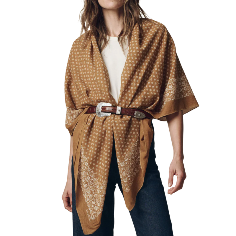 Woman wearing a brown patterned shawl over a white top and jeans on a white background