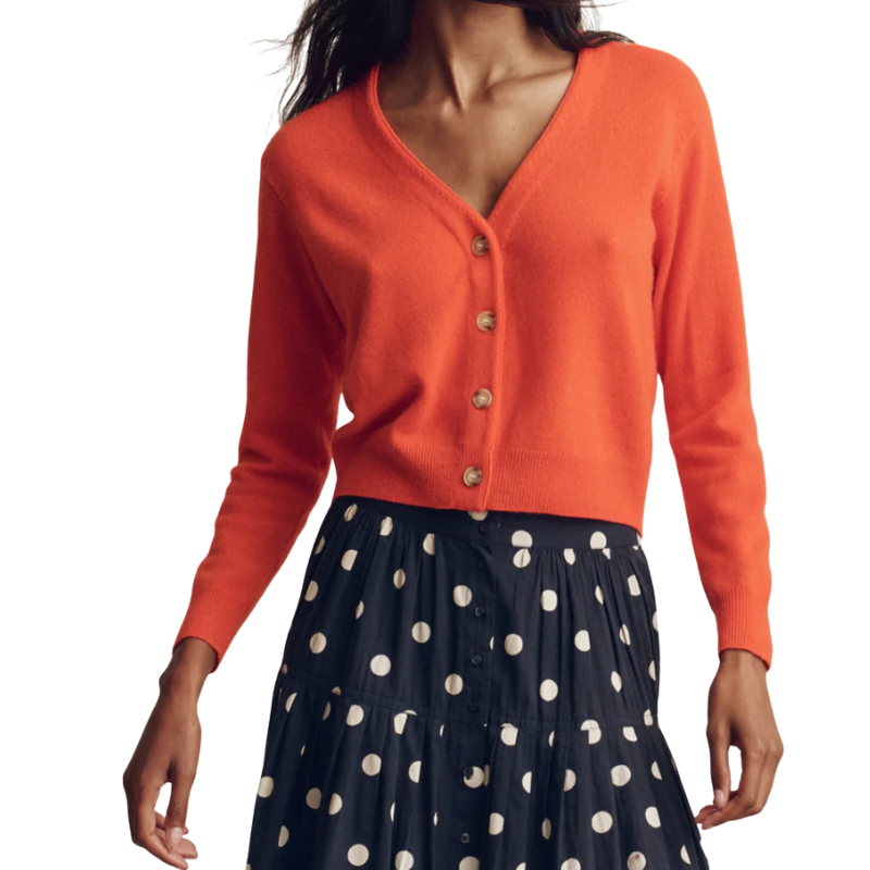 Person wearing an orange cardigan over a navy skirt with white polka dots on a white background