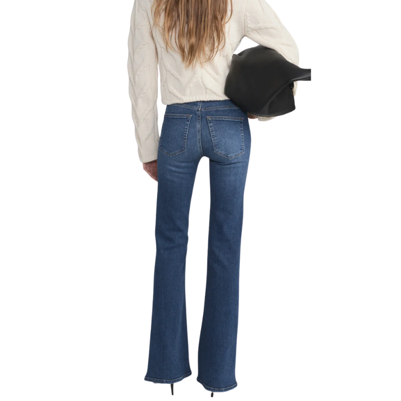 Person wearing blue jeans and a cream sweater with a black clutch on a white background