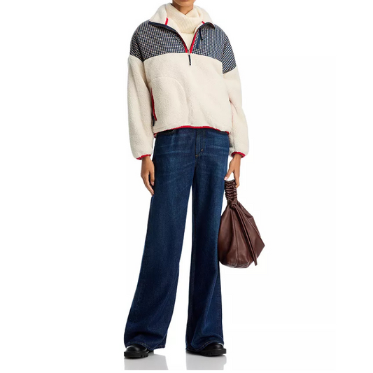 Person wearing a patterned sweater and blue jeans holding a brown bag on a white background