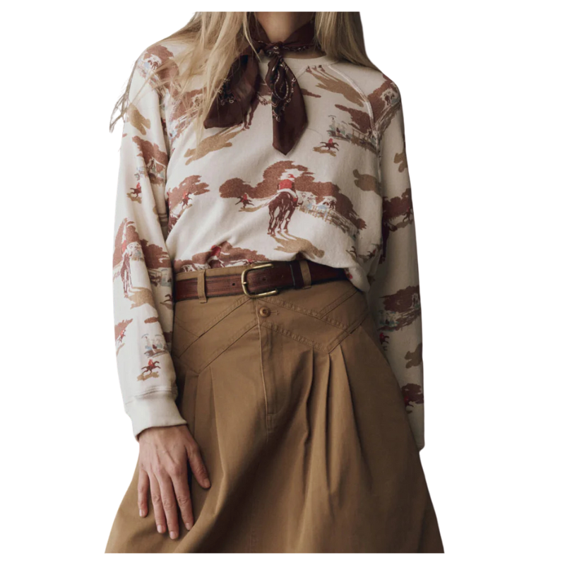 Person wearing a patterned blouse with horses and a scarf, paired with brown pants on a white background
