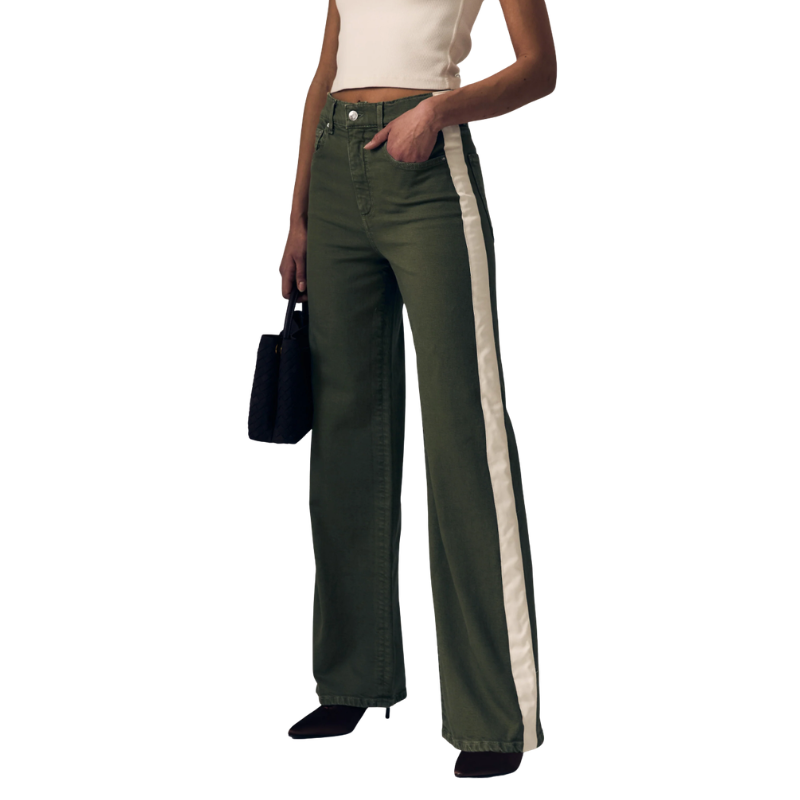 A model wearing olive green wide-leg jeans with a prominent white vertical stripe down the side, paired with a cream crop top and black heels, holding a black handbag against a white background.