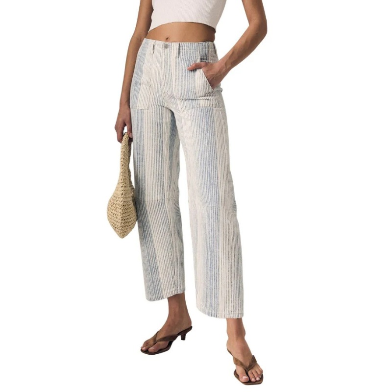 Woman wearing striped pants and a white top, holding a straw bag on a white background