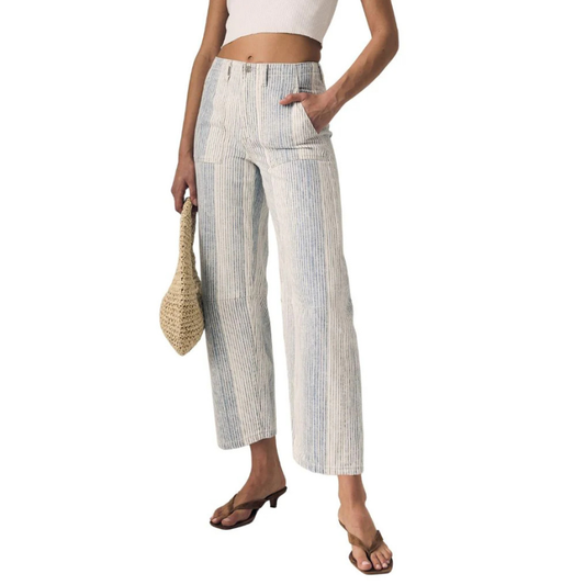 Woman wearing striped pants and a white top, holding a straw bag on a white background