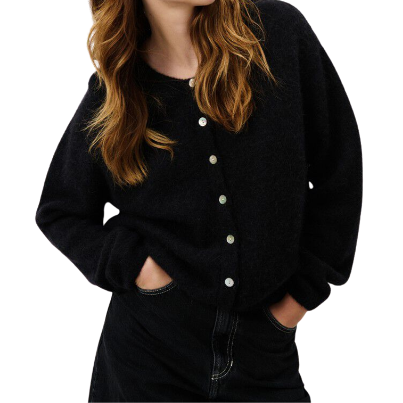 Person wearing a black cardigan with white buttons on a plain background