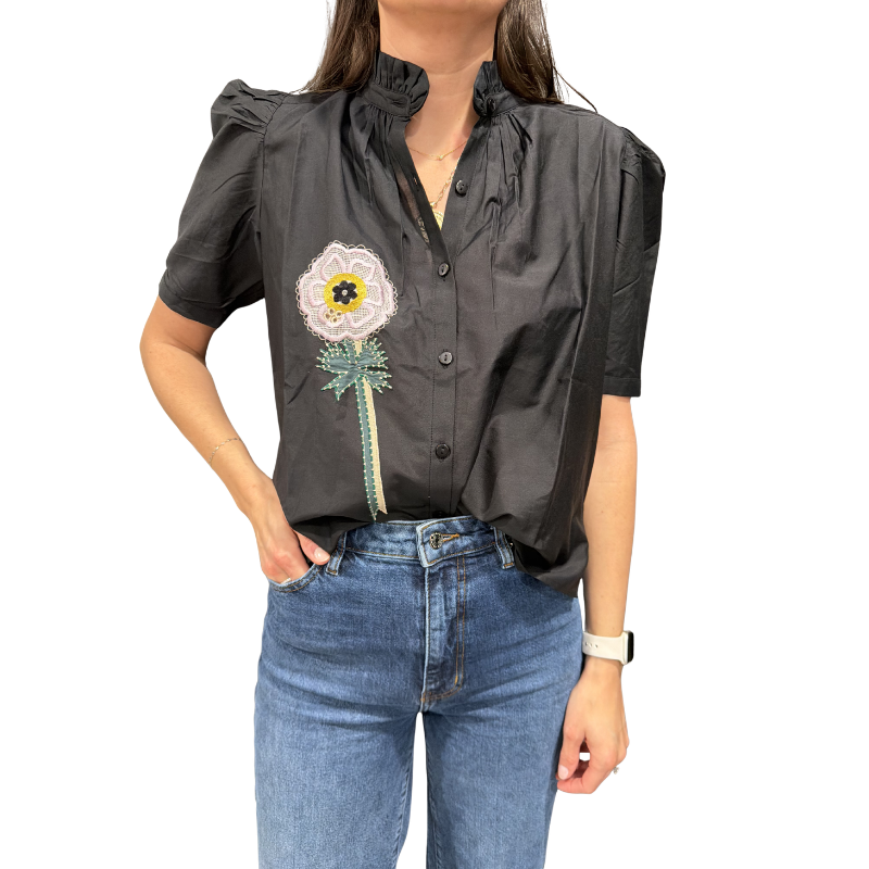 Person wearing a black blouse with floral embroidery and blue jeans on a white background